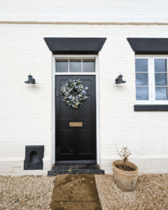 Black Churchill front door with wreath, flanked by Winston sliding sash windows, both featuring LandVac vacuum glass, on a Grade II listed brick building.