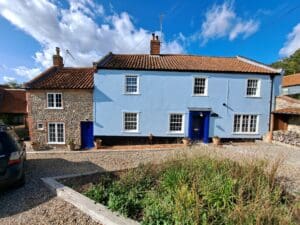 A charming heritage property featuring newly replaced windows with like-for-like frames fitted with LandVac vacuum glass. The house has a mix of traditional flint stonework and blue render, retaining its original character while benefiting from modern energy-efficient glazing. The double-hung sash windows blend seamlessly into the historical facade, preserving the aesthetic of the property in a conservation area. Windows by www.gowercroft.co.uk